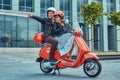 Attractive happy couple, a handsome man and female riding together on a red retro scooter in a city. Royalty Free Stock Photo