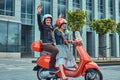 Attractive happy couple, a handsome man and female riding together on a red retro scooter in a city. Royalty Free Stock Photo