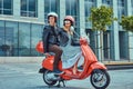 Attractive happy couple, a handsome man and female riding together on a red retro scooter in a city. Royalty Free Stock Photo