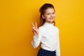 Optimistic cute girl kid showing peace gesture against bright yellow background Royalty Free Stock Photo
