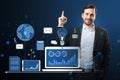 Attractive happy european businessman pointing up at financial data and accounting hologram with devices and charts on blue Royalty Free Stock Photo