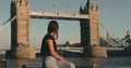 Attractive happy female admiring view of Tower Bridge in London and looking at camera, smiling