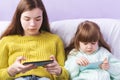 Attractive Happy girls use smartphones for entertainment while sitting on the couch during the weekend. Adorable Sisters using the Royalty Free Stock Photo