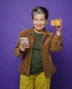 Attractive happy middle-age woman holding credit card, using cell phone for online shopping or payments isolated in studio. Online Royalty Free Stock Photo