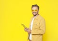 Attractive happy middle-aged man using tablet computer in hands isolated on yellow background Royalty Free Stock Photo