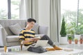 Attractive happy smart young man sitting on a floor in the living room, working on laptop computer Royalty Free Stock Photo