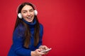 Attractive happy smiling young brunette woman wearing blue sweater isolated over red background holding and using mobile Royalty Free Stock Photo