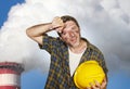 Attractive happy and tired contractor or construction worker man holding safety helmet and dirt stained face at smoking factory