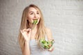 Attractive happy woman holding bowl of fresh vegetable salad in hands eating with the fork, enjoing healthy food Royalty Free Stock Photo