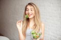 Attractive happy woman holding bowl of fresh vegetable salad in hands eating with the fork, enjoing healthy food Royalty Free Stock Photo