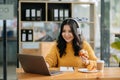 Attractive happy young Asian student studying at the college library, sitting at desk, using a laptop computer, tablet and Royalty Free Stock Photo