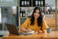 Attractive happy young Asian student studying at the college library, sitting at desk, using a laptop computer, tablet and Royalty Free Stock Photo