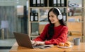 Attractive happy young Asian student studying at the college library, sitting at desk, using a laptop computer, tablet and Royalty Free Stock Photo