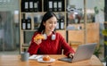 Attractive happy young Asian student studying at the college library, sitting at desk, using a laptop computer, tablet and Royalty Free Stock Photo