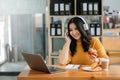 Attractive happy young Asian student studying at the college library, sitting at desk, using a laptop computer, tablet and Royalty Free Stock Photo