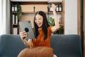 Attractive happy young Asian student studying at the college library, sitting at the sofa, using a laptop computer, tablet and Royalty Free Stock Photo