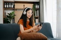 Attractive happy young Asian student studying at the college library, sitting at the sofa, using a laptop computer, tablet and Royalty Free Stock Photo