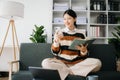 Attractive happy young Asian student studying at the college library, sitting at sofa, using a laptop computer, tablet and Royalty Free Stock Photo