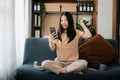 Attractive happy young Asian student studying at the college library, sitting at the sofa, using a laptop computer, tablet and Royalty Free Stock Photo