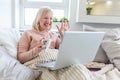 Attractive happy young woman sitting on the sofa using laptop computer, having video chat, waving, talks with her friend about Royalty Free Stock Photo