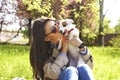 Attractive hipster young woman in sunglasses kissing jack russell terrier puppy in park, green lawn & foliage background. Funny pu