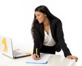 Attractive hispanic businesswoman or secretary taking notes standing leaning on office computer desk Royalty Free Stock Photo