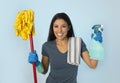 Attractive hispanic woman happy proud as home or hotel maid cleaning and housekeeping holding soap spray and mop