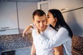 Attractive, hot, sexy brunette sits high on the kitchen furniture. Hugging boyfriend with legs passionately. Woman presses her Royalty Free Stock Photo