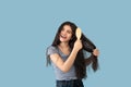 Attractive Indian teen girl brushing her long hair with wooden brush on blue studio background