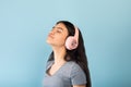 Attractive Indian teen girl enjoying her new stereo headset, listening to music with closed eyes over blue background Royalty Free Stock Photo