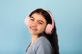 Indian teen girl in casual wear listening to music in pink wireless headphones, enjoying cool song on blue background Royalty Free Stock Photo