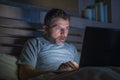 Attractive internet addict man in shock and surprise networking late night on bed surprised face expression working with laptop Royalty Free Stock Photo