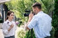 Journalist holding microphone and cameraman shooting her outside