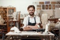 Portrait of attractive joyful bearded male sculptor which sitting on the workshop interior background and looks at the