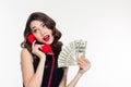 Attractive joyful curly female holding money and talking on telephone