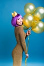 Attractive joyful young woman in luxury fashionable dress celebrating great party on blue background. Golden balloons