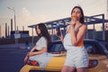 Attractive ladies in casual clothes eating pizza, enjoying soda water in glass bottles, posing near yellow car on Royalty Free Stock Photo