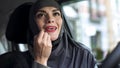 Attractive lady in hijab applying red lipstick in car, make-up beauty, feminism Royalty Free Stock Photo