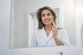 Joyful young woman using golden facial massager in bathroom