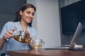 Beautiful young woman pouring tea and using laptop Royalty Free Stock Photo