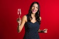 Attractive latin woman smiling and holding glass of champagne or wine on red studio background. Party 2020 mood Royalty Free Stock Photo