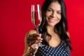 Attractive latin woman smiling and holding glass of champagne or wine on red studio background. Party 2020 mood Royalty Free Stock Photo