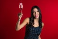 Attractive latin woman smiling and holding glass of champagne or wine on red studio background. Party 2020 mood Royalty Free Stock Photo