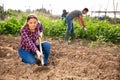 Latina woman tilling soil with hoe in garden
