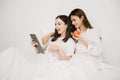 Attractive lesbian couple use mobile phone, tablet watch movie on bed. Beautiful sibling in pajamas lying down with blanket in Royalty Free Stock Photo