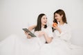 Attractive lesbian couple use mobile phone, tablet watch movie on bed. Beautiful sibling in pajamas lying down with blanket in Royalty Free Stock Photo