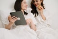 Attractive lesbian couple use mobile phone, tablet watch movie on bed. Beautiful sibling in pajamas lying down with blanket in Royalty Free Stock Photo