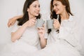 Attractive lesbian couple use mobile phone, tablet watch movie on bed. Beautiful sibling in pajamas lying down with blanket in Royalty Free Stock Photo