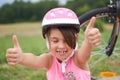 Attractive little cyclist giving thumbs up. Happy joyful little girl with bicycle on the background gesturing thumb up Royalty Free Stock Photo