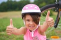 Attractive little cyclist giving thumbs up. Happy joyful little girl with bicycle on the background gesturing thumb up Royalty Free Stock Photo